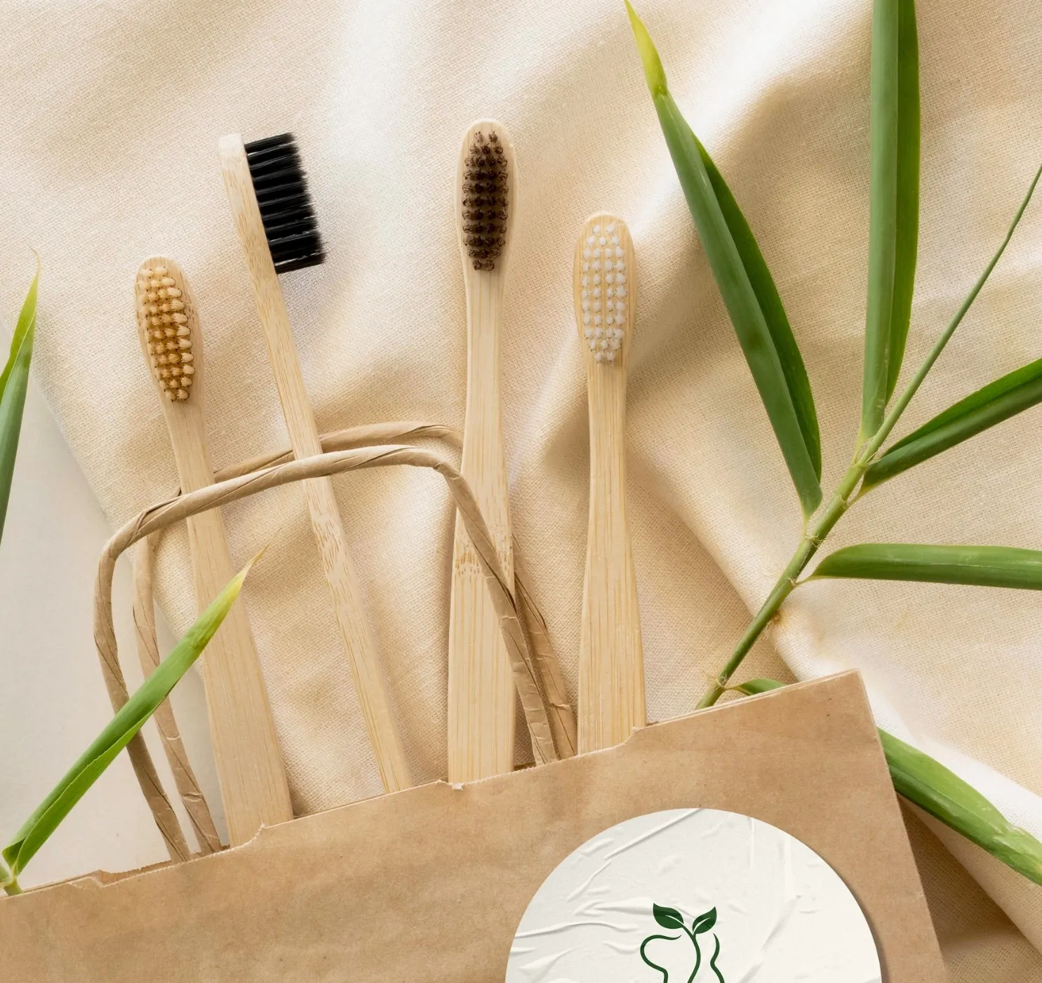 Bamboo toothbrushes and a paper bag on natural linen, beside a bamboo sprig